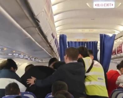 Passengers and crew restraining two fighting passengers on an airplane.