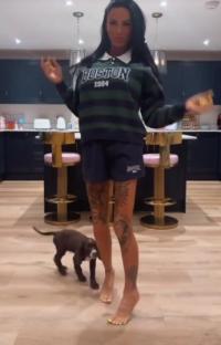 Woman in a striped sweatshirt and shorts kicks a small dog out of the way.