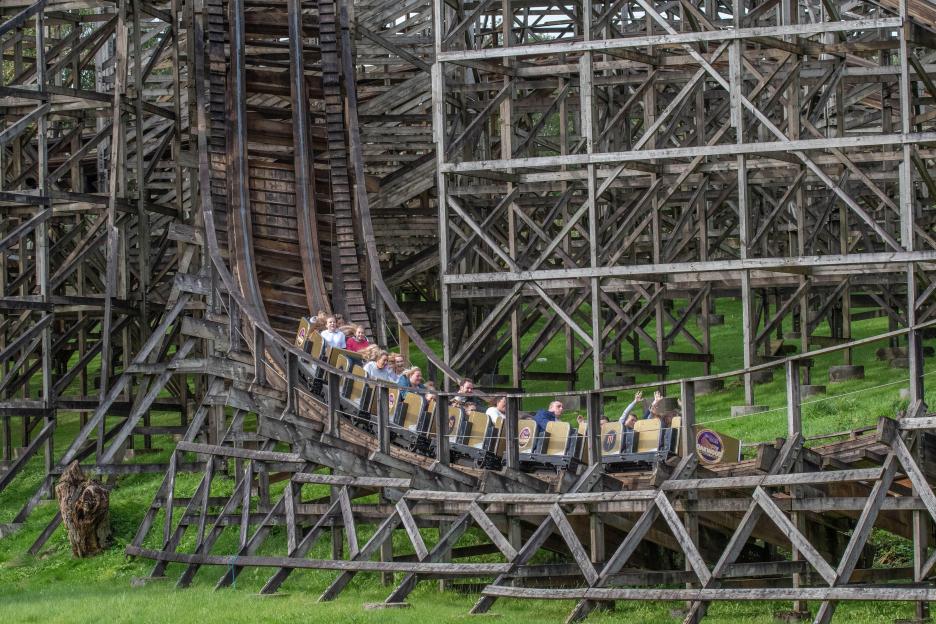 Rollercoaster car full of people going down a wooden track.