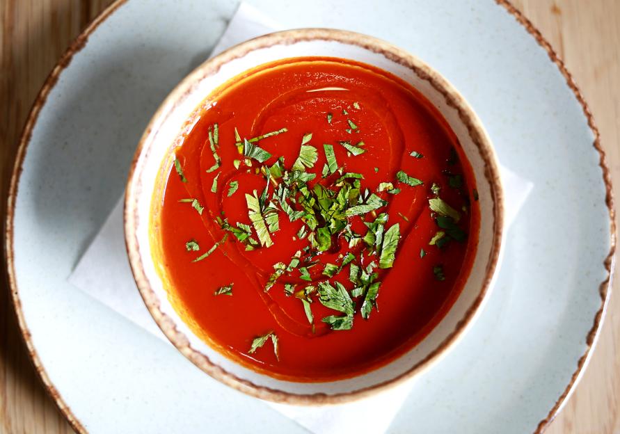 Bowl of tomato soup garnished with basil and olive oil.