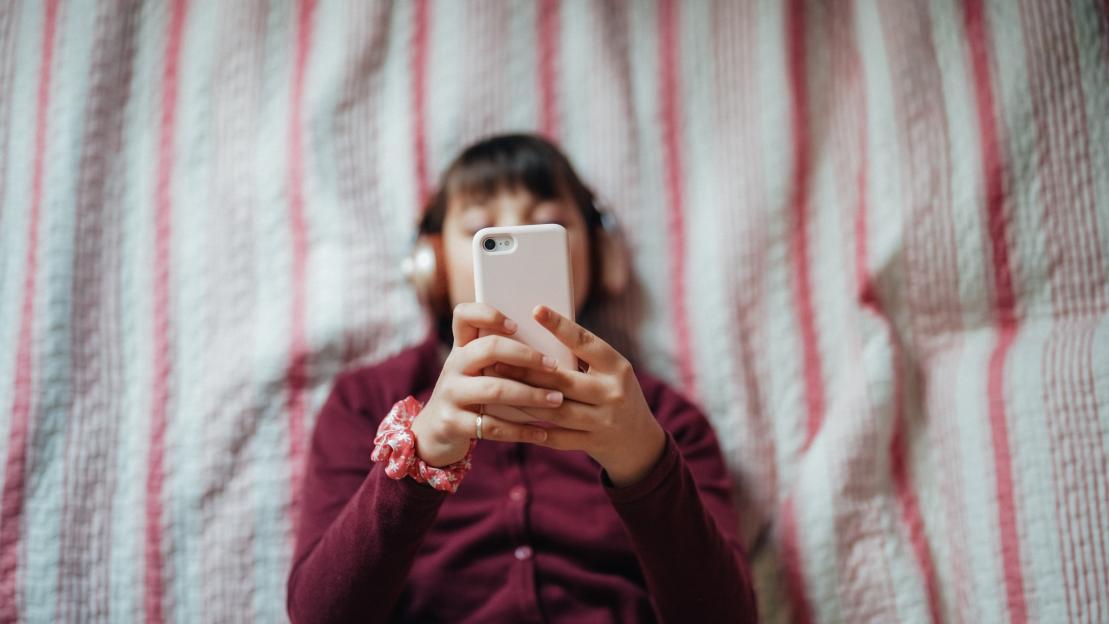 Girl lying in bed listening to music on her phone.