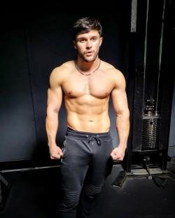 Shirtless man flexing in gym.
