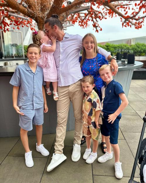 A man kisses his young daughter while standing with his other children.