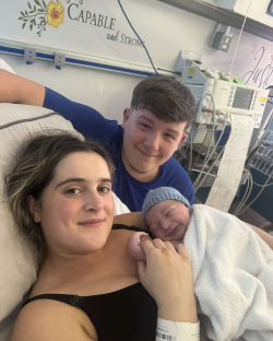 New parents holding their newborn baby in a hospital room.