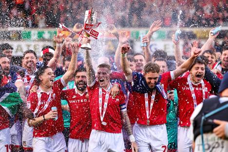 Wrexham AFC players celebrating a victory and lifting a trophy.