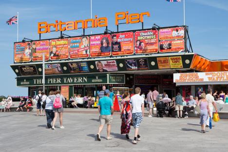 Britannia Pier in Great Yarmouth, England, showing crowds of people and numerous entertainment advertisements.
