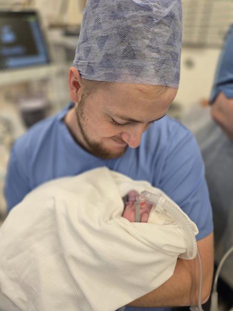 Man in scrubs holding a newborn baby connected to a breathing tube.