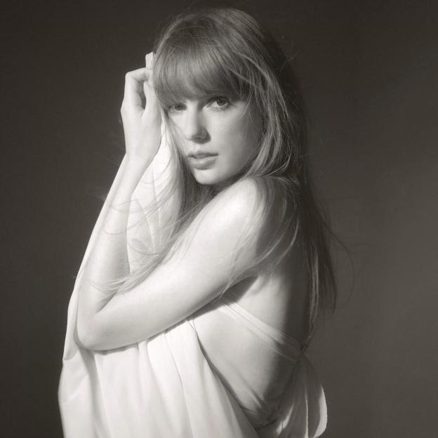 Taylor Swift with light hair looking at the camera with her hands near her face.