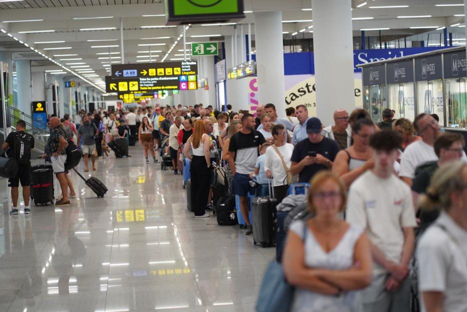 Travelers and their luggage stand in a long, crowded queue at Palma Airport.