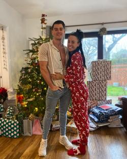 Couple embracing in front of a Christmas tree and presents.