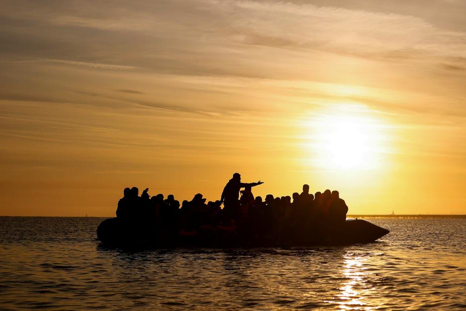 Silhouetted migrants in an inflatable boat at sunset.