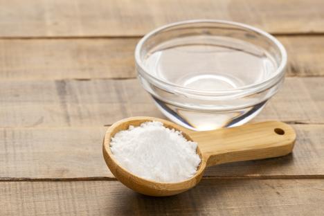 Baking soda in a wooden spoon and water in a glass bowl.