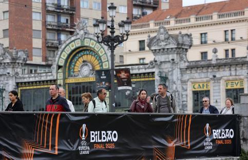 People in Bilbao, Spain, stand behind a Europa League Final 2025 banner.