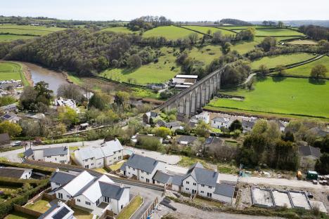 Aerial view of a partially completed housing estate near a viaduct and river.