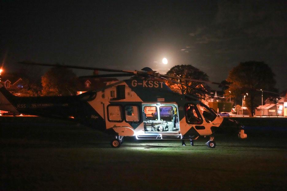 A KSS air ambulance helicopter, G-KSST, with open doors on a grassy field at night, under a bright moon.