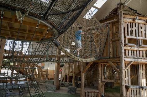 Person crossing a rope bridge on a wooden playground structure.