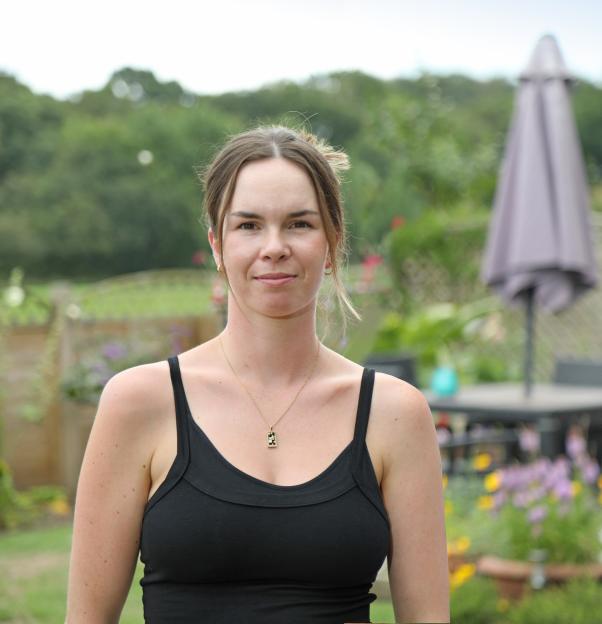 Woman in a black tank top in a garden.