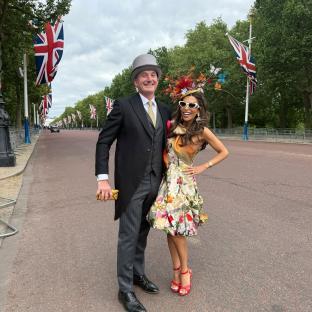 Panthea Parker and a man in formal wear stand on a street lined with British flags.