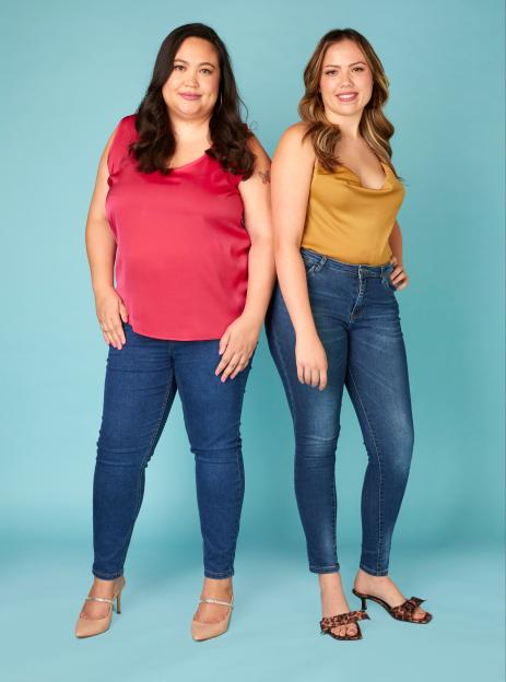 Michelle and Bella Lopez, a mother and daughter, pose in jeans and satin tops against a blue background.