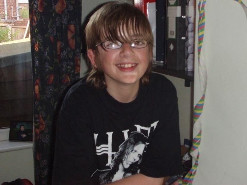 Andrew Gosden, a 14-year-old boy, with shoulder-length brown hair, glasses, and a black t-shirt.