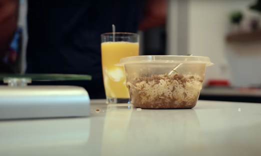 Rice and meat dish in a plastic container, next to a glass of orange juice.