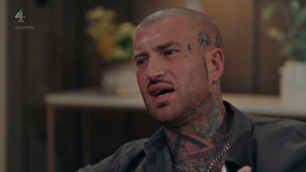 A tattooed man with a nose ring and earrings speaks animatedly.