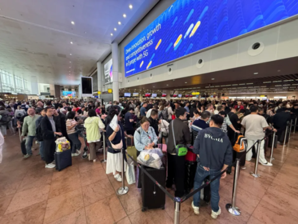A crowded airport hall with people waiting in long lines.