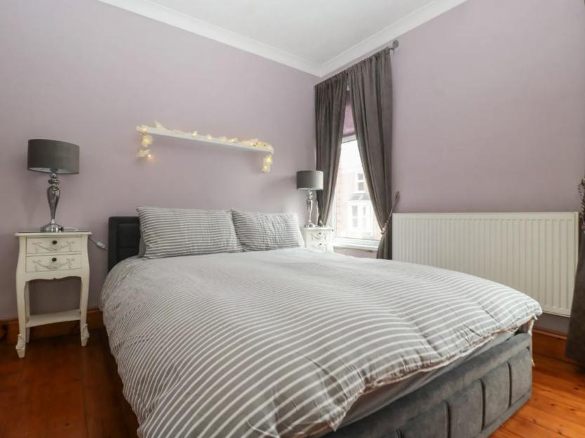 A bedroom in Lush House with a double bed, purple walls, two bedside tables with lamps, a window, and a radiator.