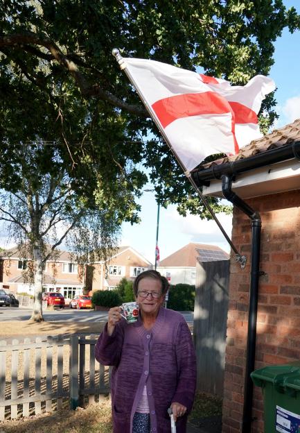 Woman holding a mug stands in front of a flagpole with an English flag.