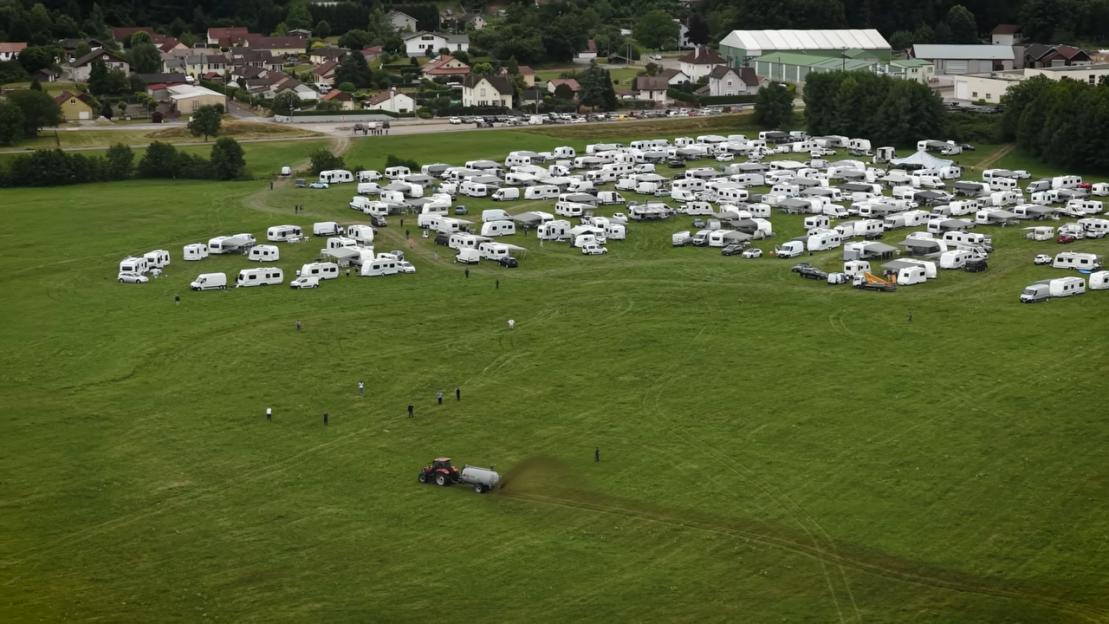 Aerial view of a tractor spreading manure near numerous RVs parked in a field.