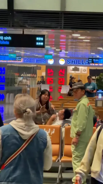 A group of people waiting in what looks like an airport lounge with a sign in Vietnamese, Korean, and Chinese that says "Toilets".