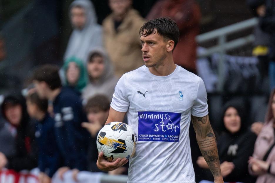 Soccer player holding a ball, wearing a white jersey with a charity logo.