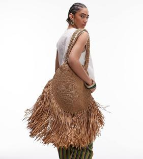 Woman holding large fringed straw tote bag.