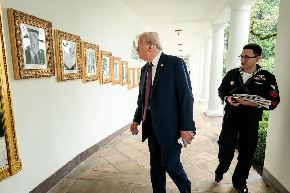 Donald Trump walks past framed photos of US presidents on a White House hallway.