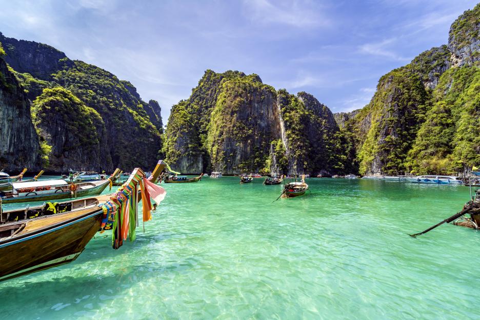 A person with dark hair and tattoos on their neck and chest looks into the camera, a comment overlaying the upper left of the image asks how they can afford to live in Thailand.