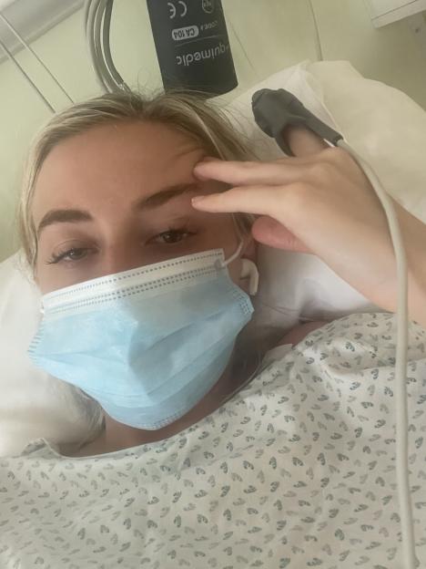 Woman in hospital bed wearing a face mask.