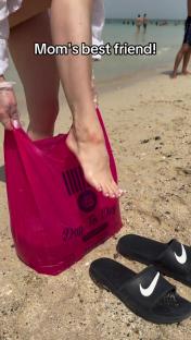 Woman's feet near pink bag and sandals on beach.