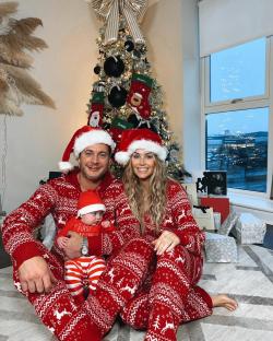 Family in matching Christmas pajamas in front of a decorated Christmas tree.