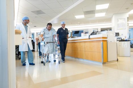 A transplant recipient walks down a hospital hallway with two doctors.