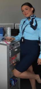 Flight attendant in uniform next to a beverage cart.