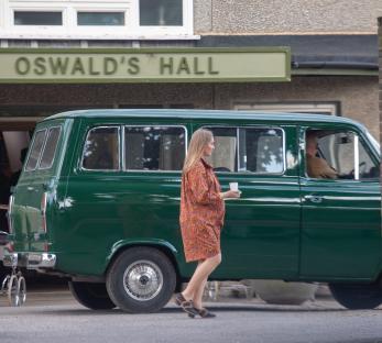 A woman walks past a vintage green van in front of Oswald's Hall.
