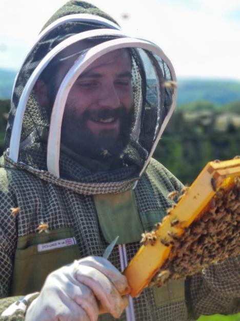 A beekeeper smiling while inspecting a honeycomb.