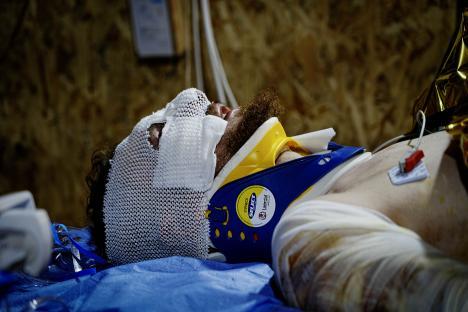 A wounded soldier in a neck brace and bandages awaits an ambulance.