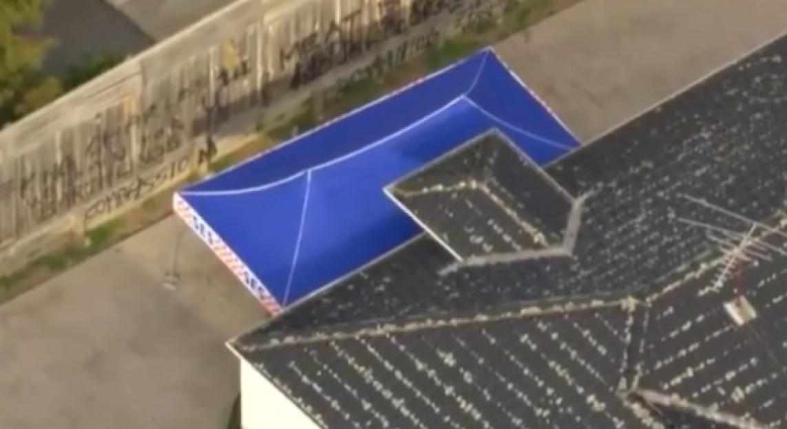 Aerial view of a house with a blue tarp and graffiti-covered wall.