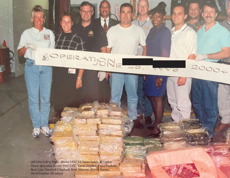 A group of thirteen people standing behind a banner that reads "OPERATION" and "2000+", with large quantities of packaged drugs in front of them.
