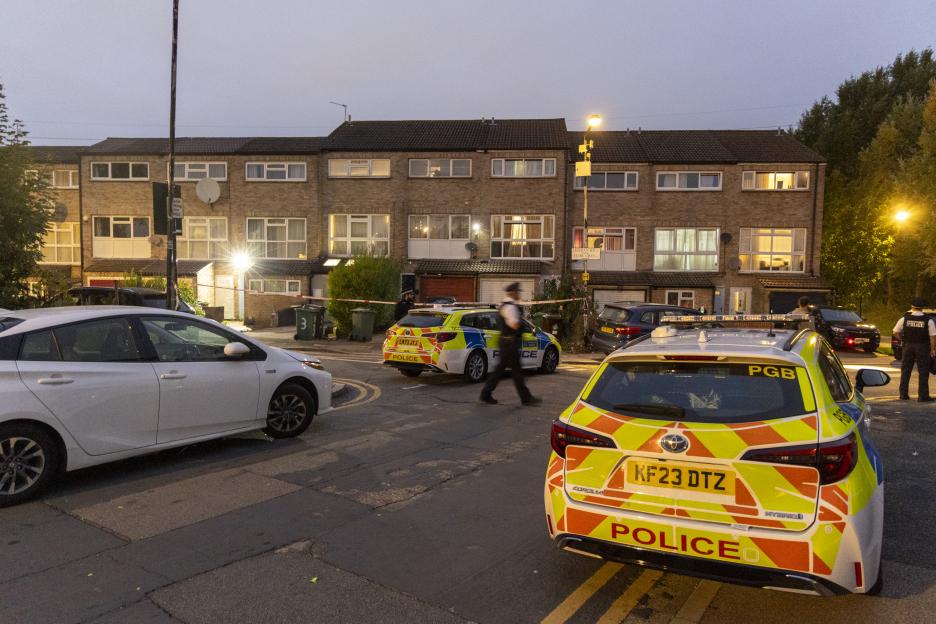 Police officers and two patrol cars at a crime scene with a cordon in front of terraced houses in Walthamstow, London.