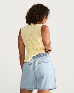 Woman from behind wearing a yellow eyelet top and light blue denim shorts.