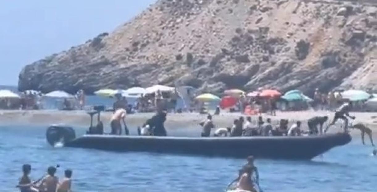 A boat arrives at a beach carrying a large group of people.