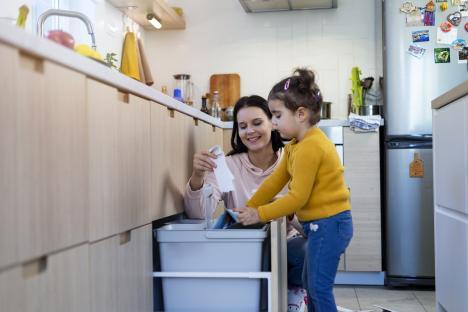 A mother and daughter sorting recyclables in their kitchen.