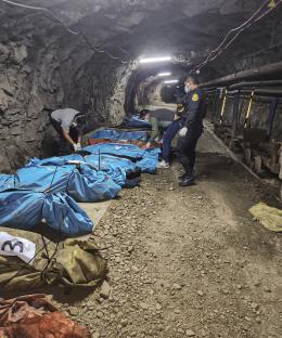 Police officers in a mine next to the bodies of thirteen workers covered in blue tarps.